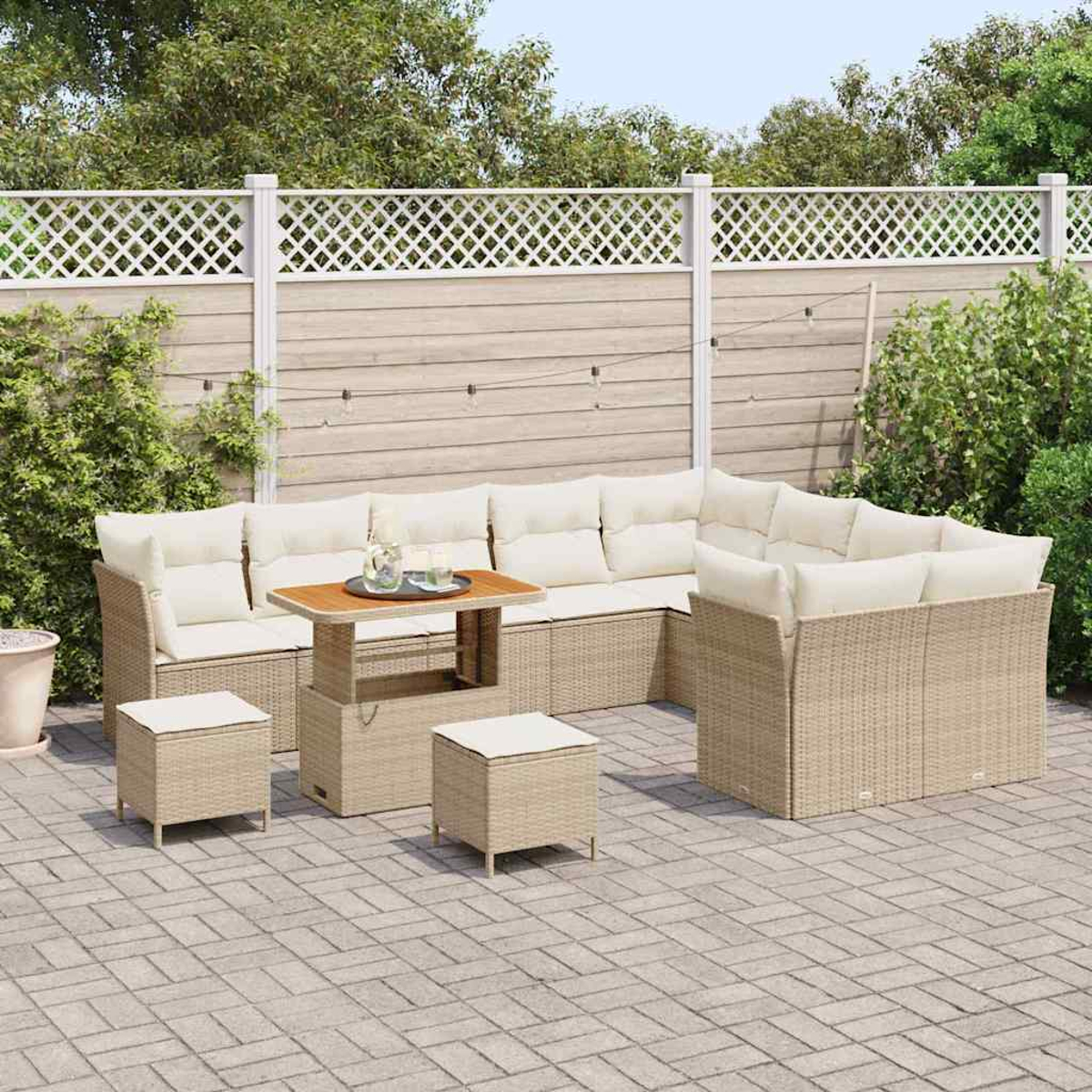 Garten-Set: beigefarbenes Korbmöbel-Sofa mit weißen Kissen, Holztisch, zwei Ottomanen und weißem Zaun im Hintergrund.