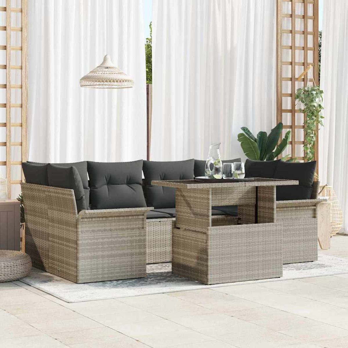 Juego de muebles de patio. Cojines grises sobre asientos estilo mimbre. Mesa con vasos y jarra. Cortinas blancas y lámpara colgante.