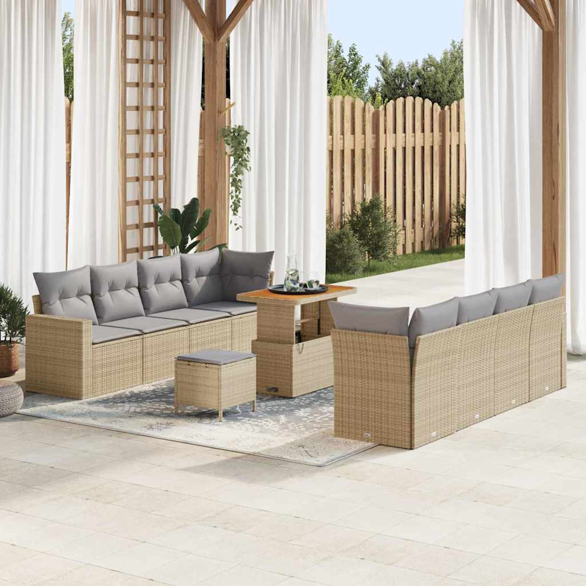 Außenbereich mit Sitzgelegenheiten. Beige Korbsessel mit grauen Kissen, ein Tisch und ein Hocker auf einem Teppich. Weiße Vorhänge und Holzzaun im Hintergrund.