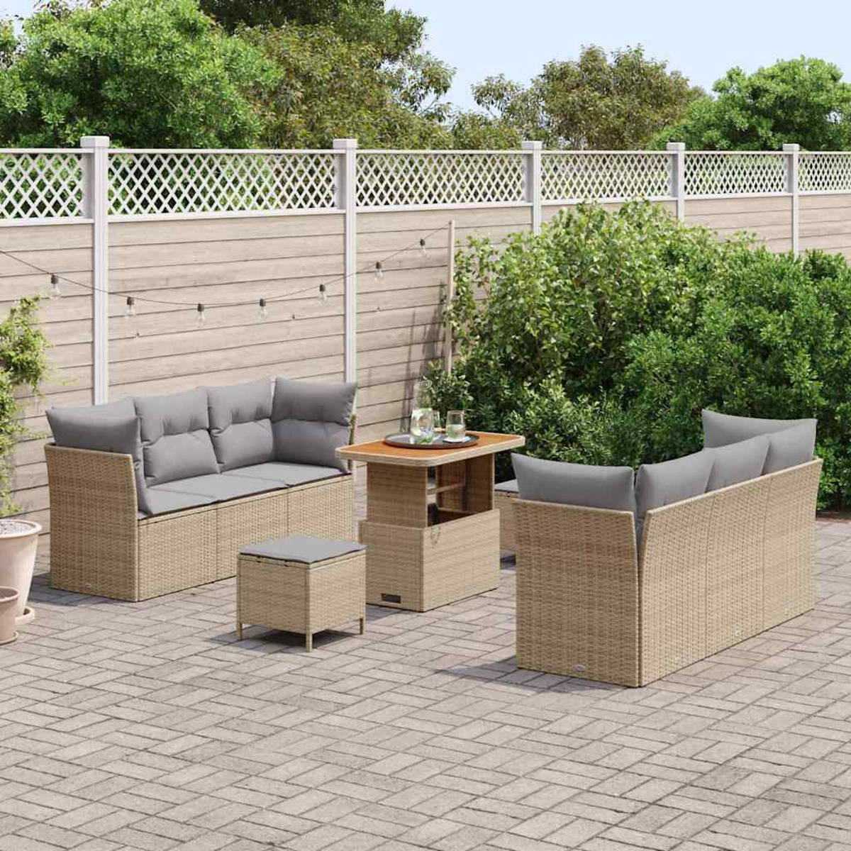 Terrassenset: zwei Sofas, ein Tisch und ein kleiner Hocker. Kissen sind grau. Auf einer Backsteinterrasse mit Zaun und Grün.