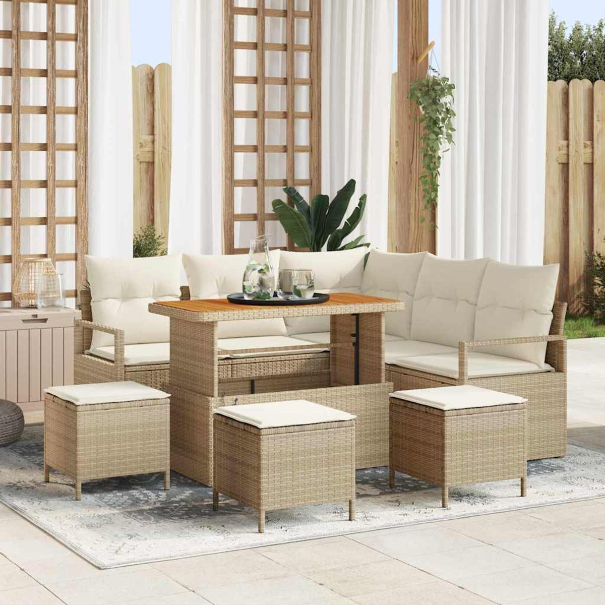 Set da patio esterno. Include tavolo, divano e pouf in beige intrecciato. Cuscini bianchi. Tende e traliccio in legno sullo sfondo.