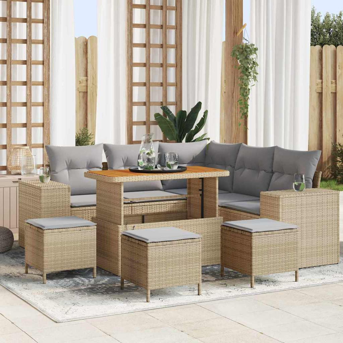 Set divano in rattan da esterno con cuscini, tavolo e pouf su un tappeto. Include tende, piante e recinzione in legno.