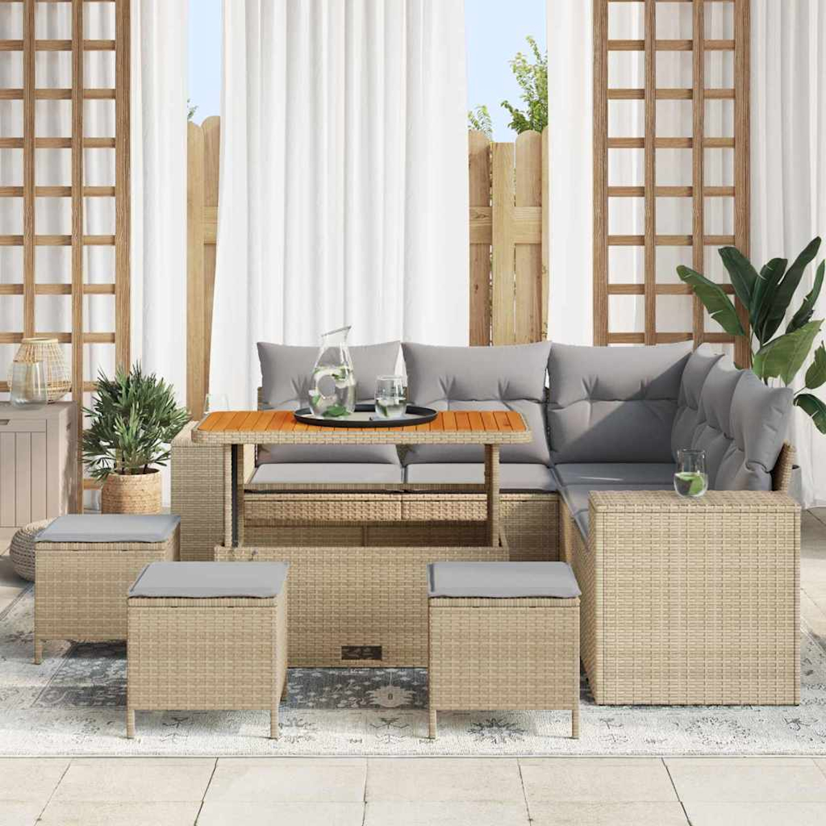 Set di mobili da esterno in vimini con cuscini grigi. Include un tavolo con bevande, pouf e divano componibile. Piante e tende sullo sfondo.