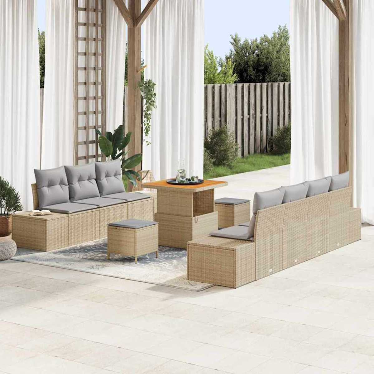 Terrassenset mit beigen Möbeln, grauen Kissen und Holztisch. Weiße Vorhänge und Grün im Hintergrund.