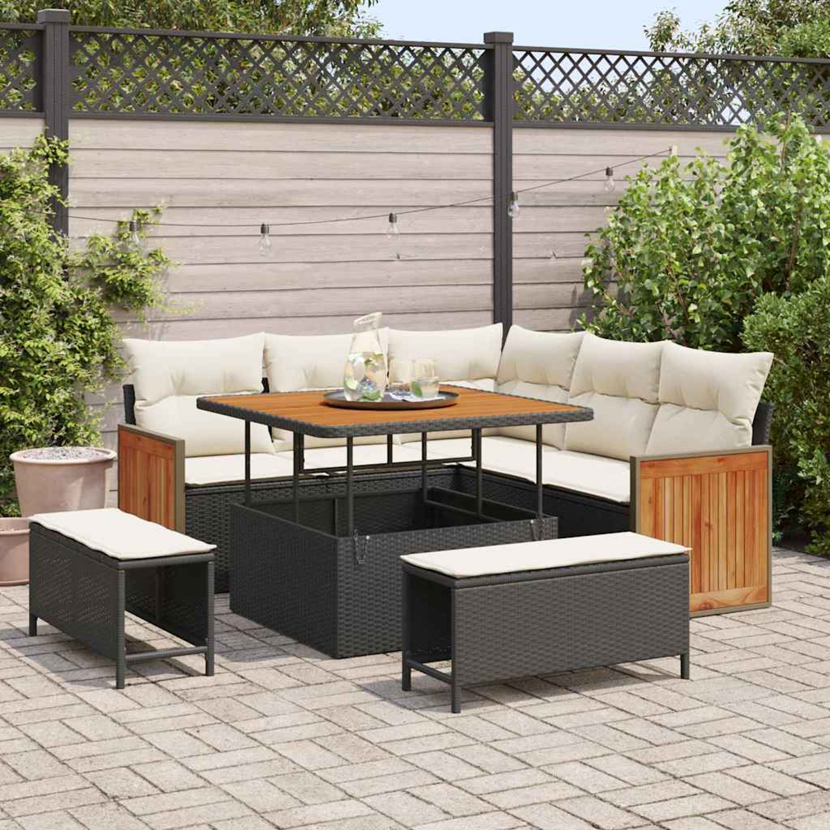 Gartenmöbel-Set mit Ecksofa, Tisch und zwei Ottomanen auf einer Backsteinterrasse mit Holzzaun im Hintergrund.