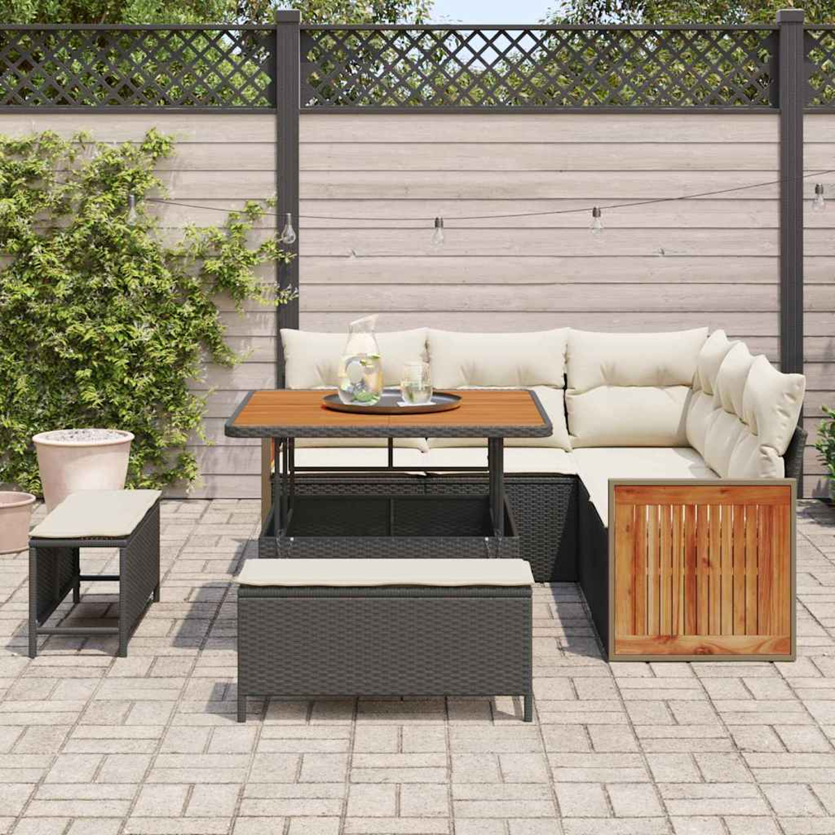 Terrassenset mit Tisch, Ecksofa und Bank. Enthält Getränke auf einem Tablett. Zaun und Grün im Hintergrund.