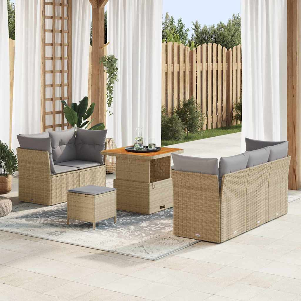Terrassenset mit Korbmöbeln, grauen Kissen und einem Holztisch. Im Hintergrund Vorhänge, ein Zaun und Bäume.