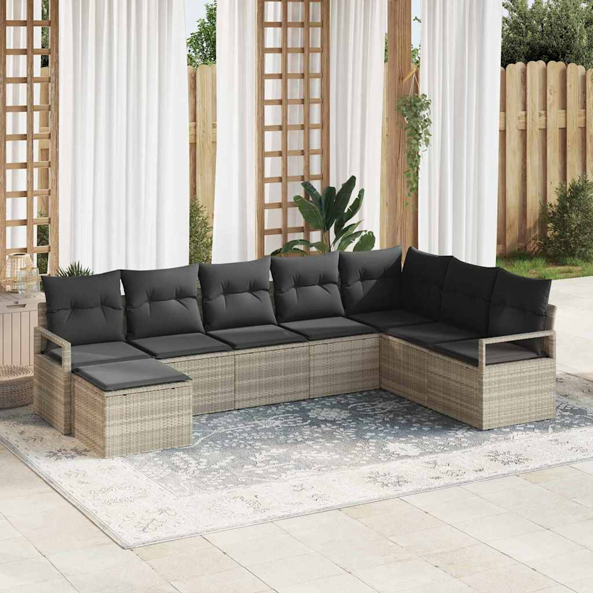 Ein Ecksofa im Freien mit grauen Kissen steht auf einem gemusterten Teppich. Weiße Vorhänge und Holzgitter sind im Hintergrund.