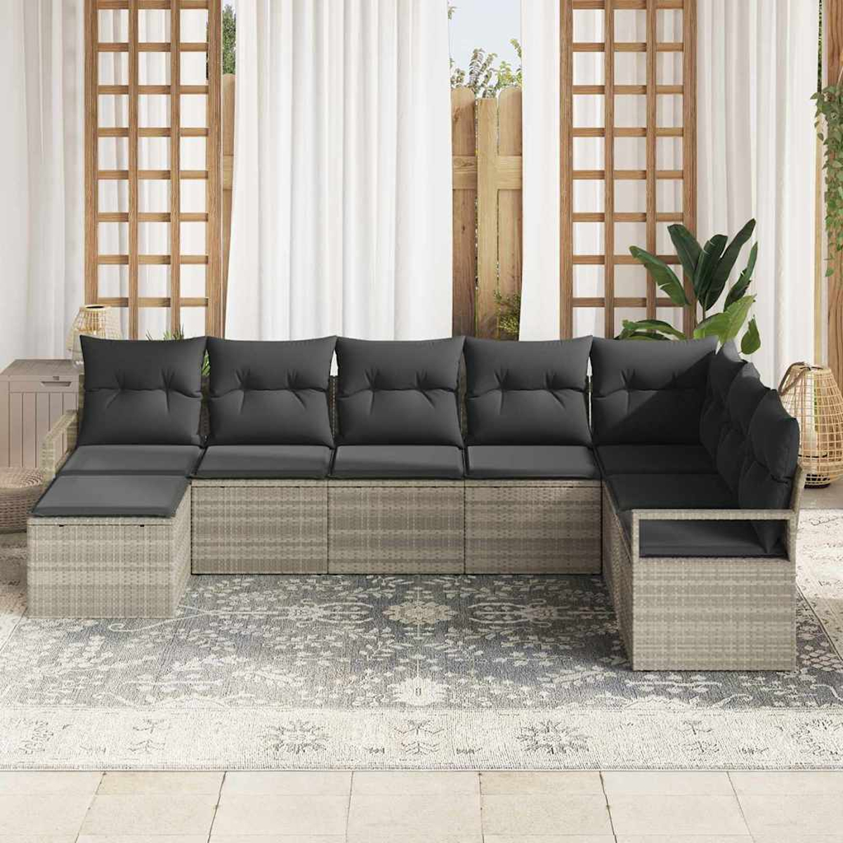 Ein Ecksofa im Freien mit dunkelgrauen Kissen steht auf einem gemusterten Teppich. Weiße Vorhänge und Holzgitter im Hintergrund.