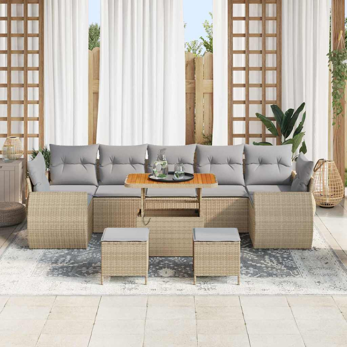 Outdoor-Rattansofa-Set mit grauen Kissen, kleinen Tischen und Hockern. Weiße Vorhänge und ein Teppich vervollständigen die Terrasse.