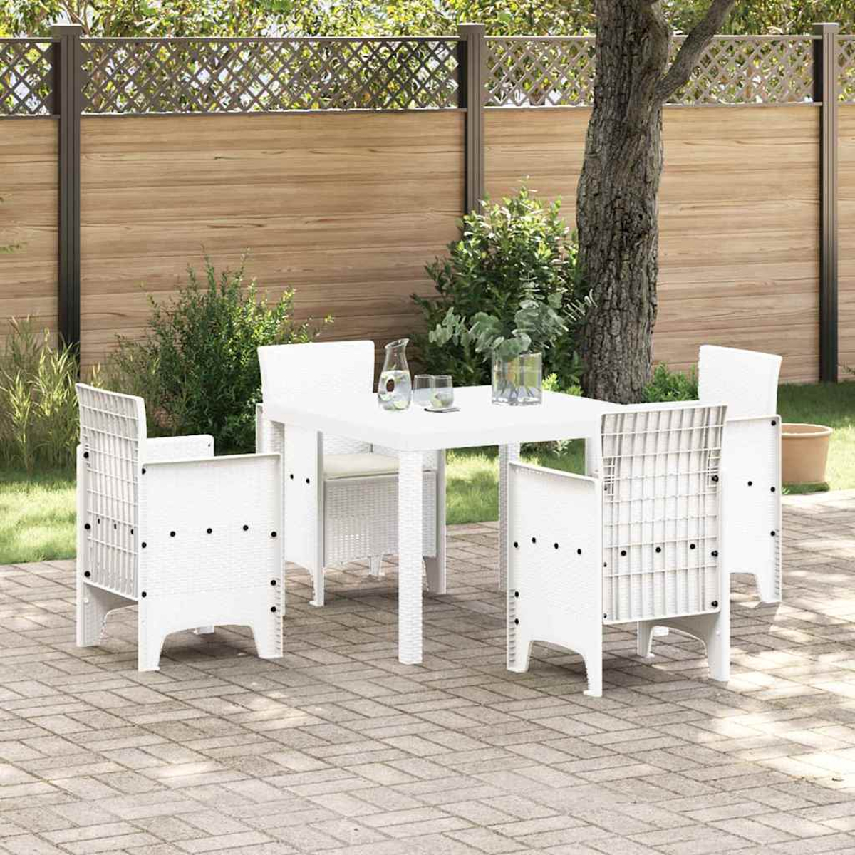 Juego de patio blanco con mesa, sillas y bebidas. En un patio de ladrillo en un patio trasero con valla de madera y árbol.