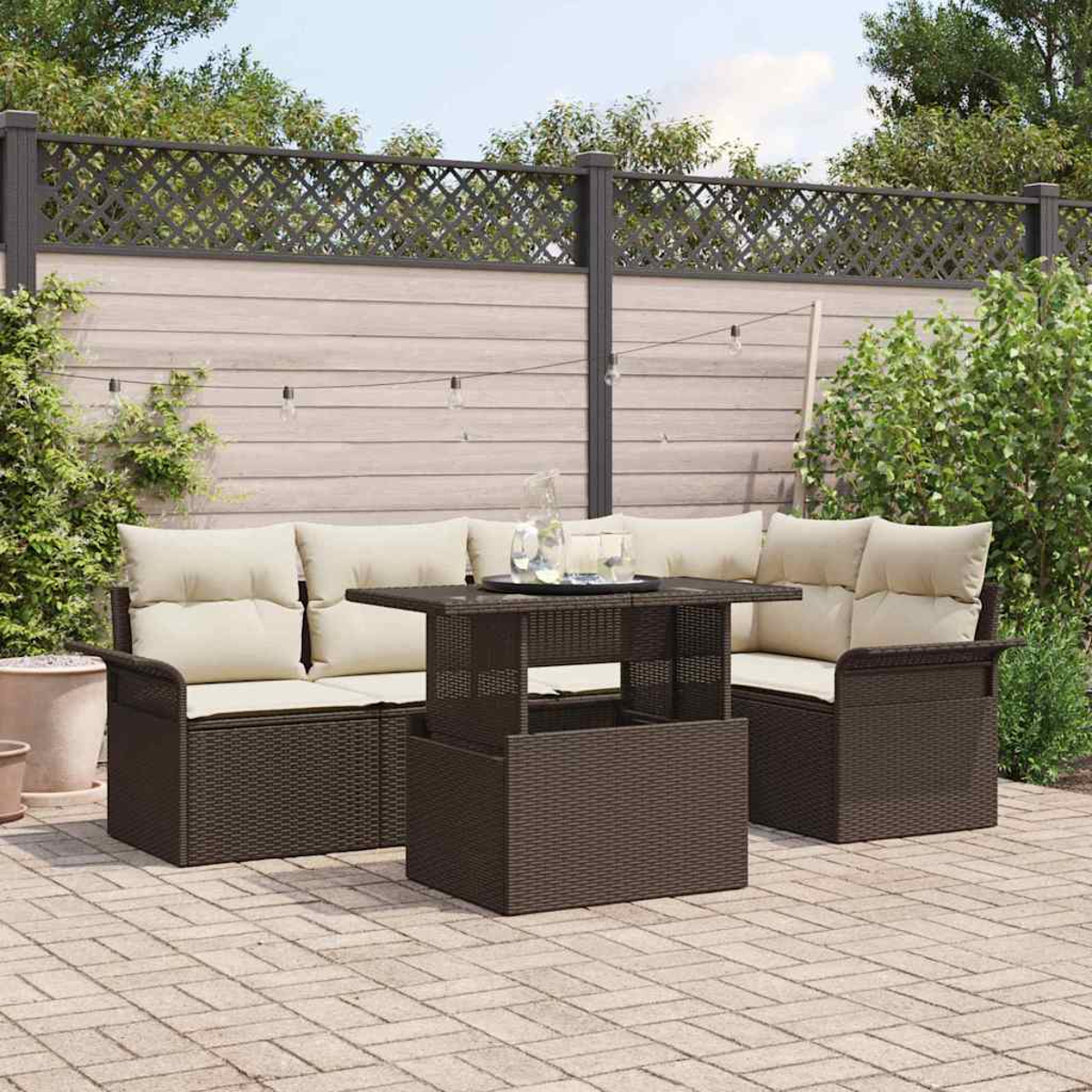 Garten-Terrassenset. Braunes Korbmöbel mit cremefarbenen Kissen, Tisch und Stühlen. Vor einem Zaun und Grün. Ziegelpflasterung.