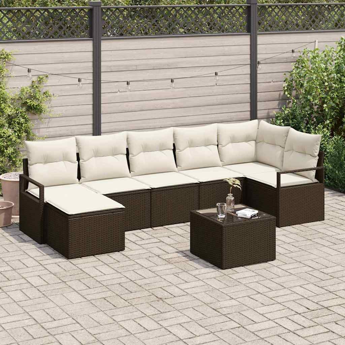 Ein braunes Outdoor-Ecksofa aus Korbgeflecht mit cremefarbenen Kissen und einem passenden Couchtisch. Auf einer Ziegelterrasse mit Zaun und Pflanzen.