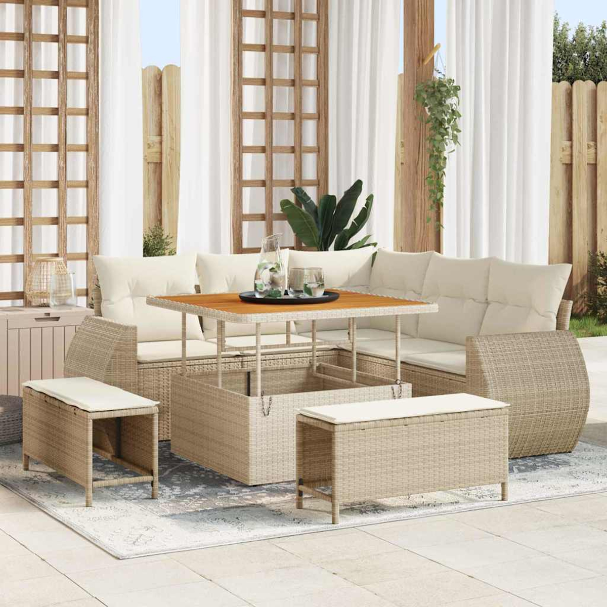 Zona de estar al aire libre con un sofá de mimbre marrón claro, mesa y bancos. Cortinas blancas y enrejado de madera al fondo.