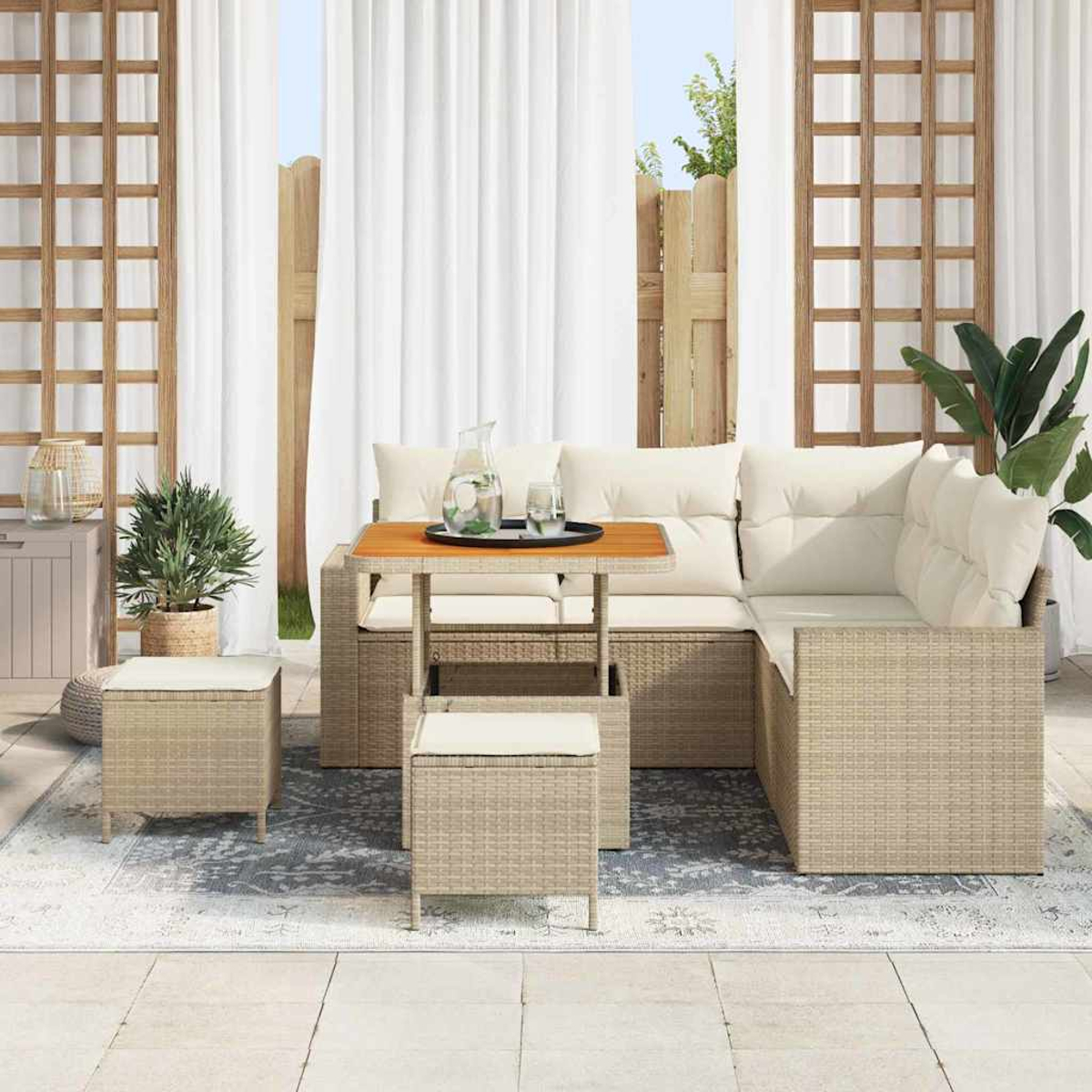 Outdoor-Terrassenset mit einem Korbmöbelsofa, passenden Hockern und einem kleinen Tisch. Weiße Vorhänge und ein Holzzaun sind im Hintergrund.