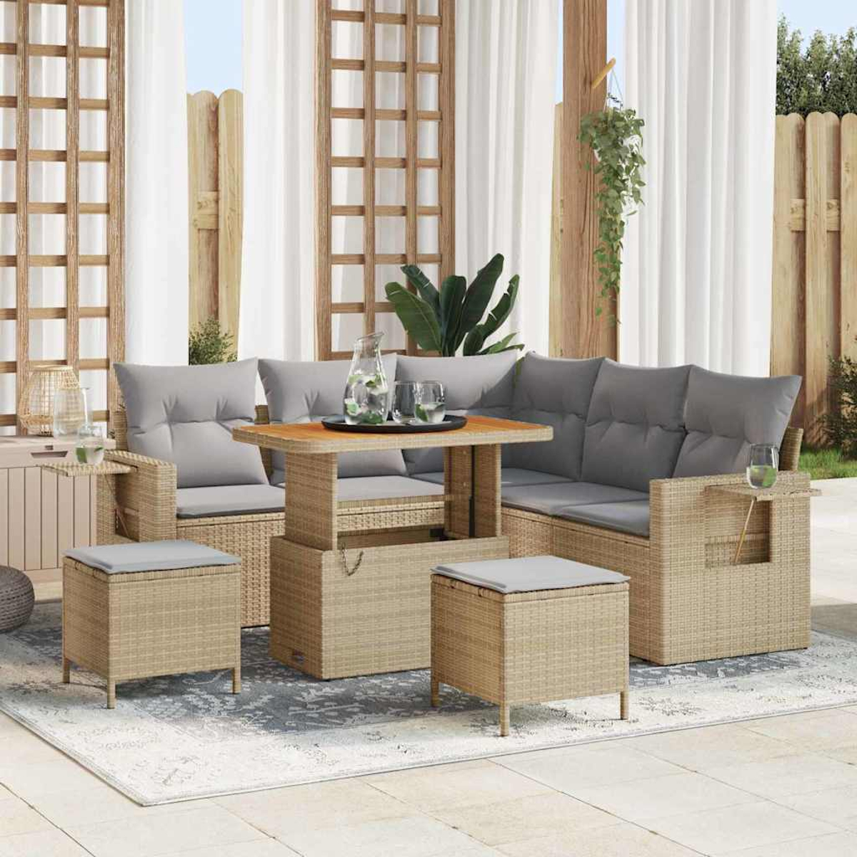 Garten-Rattan-Möbelset mit grauen Kissen, einem Holztisch und zwei Ottomanen auf einem gemusterten Teppich, Vorhänge im Hintergrund.