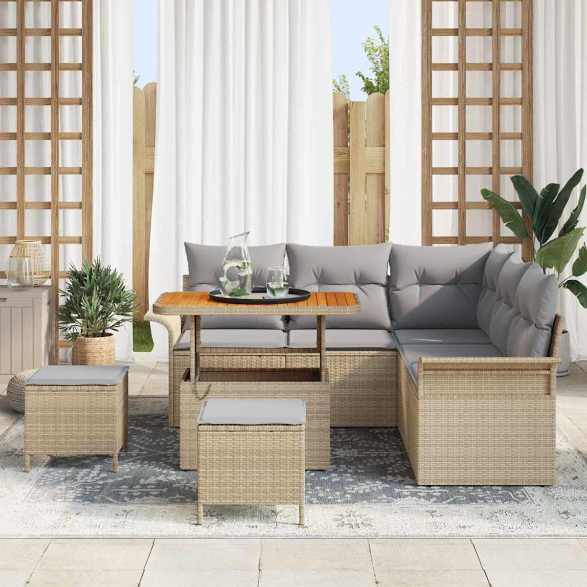 Outdoor-Wickertisch mit grauen Kissen, Tisch mit Tablett, zwei Ottomanen, Topfpflanzen und transparenten Vorhängen.