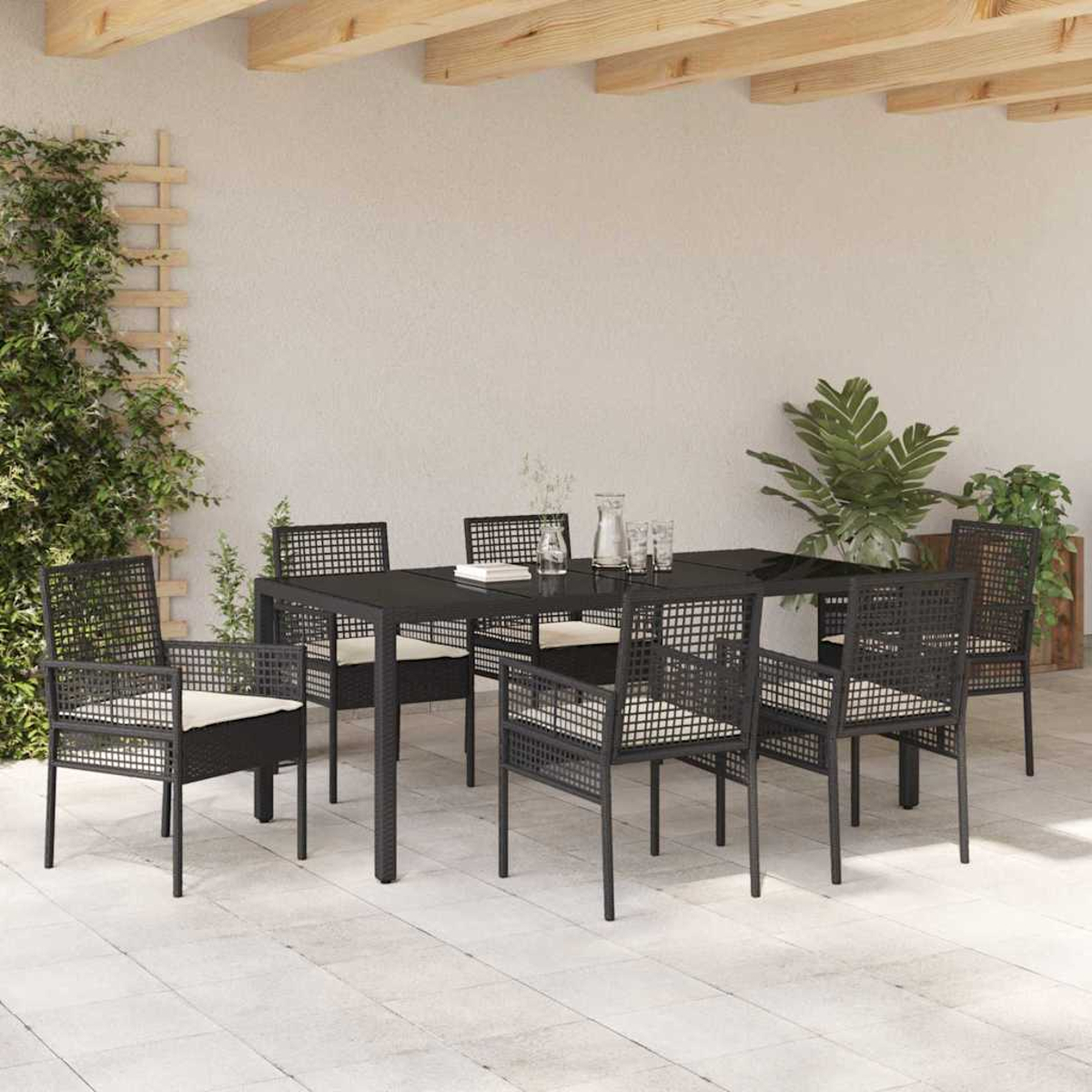 Essgruppe im Freien mit schwarzem Tisch, Stühlen und cremefarbenen Kissen. Pflanzen und eine hellfarbige Wand im Hintergrund.