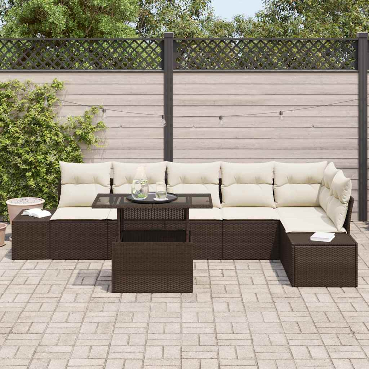 Outdoor-Sofa aus Korbgeflecht mit cremefarbenen Kissen, Couchtisch mit Glasplatte und Holzzaun im Hintergrund.
