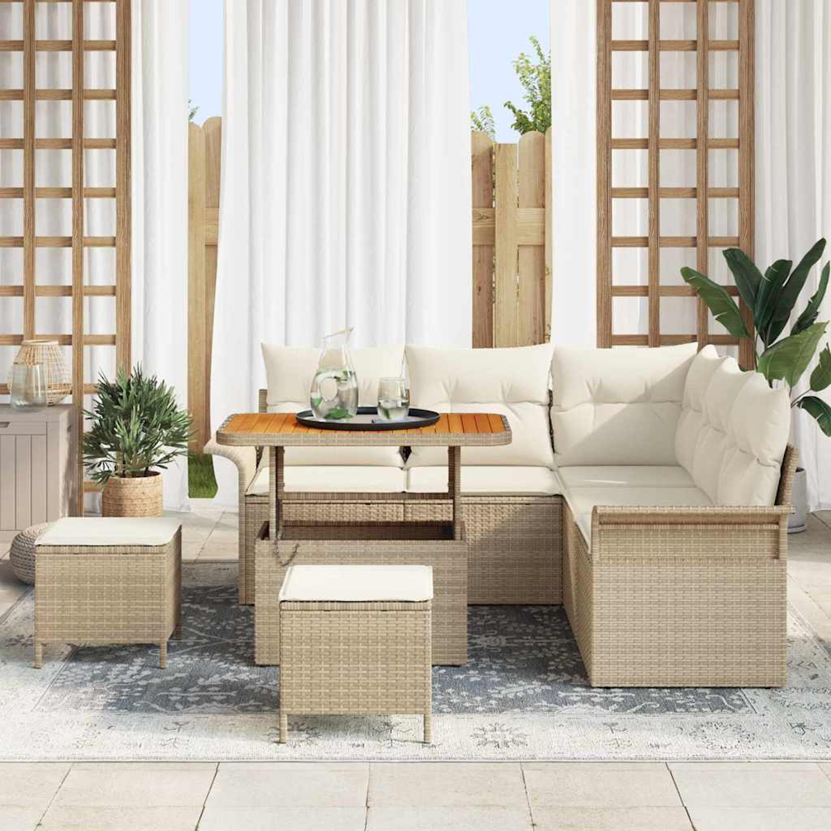 Set da patio esterno con mobili in vimini, cuscini color crema, tavolo in legno e piante. Lo sfondo presenta tende bianche e una recinzione in legno.