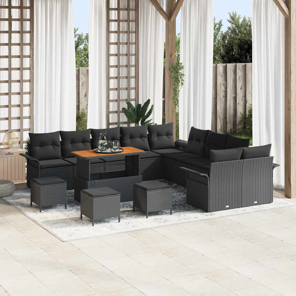 Terrassenset mit schwarzen Kissen, einem Holztisch und passenden Hockern. Das Set steht auf einem Teppich, in der Nähe weißer Vorhänge.
