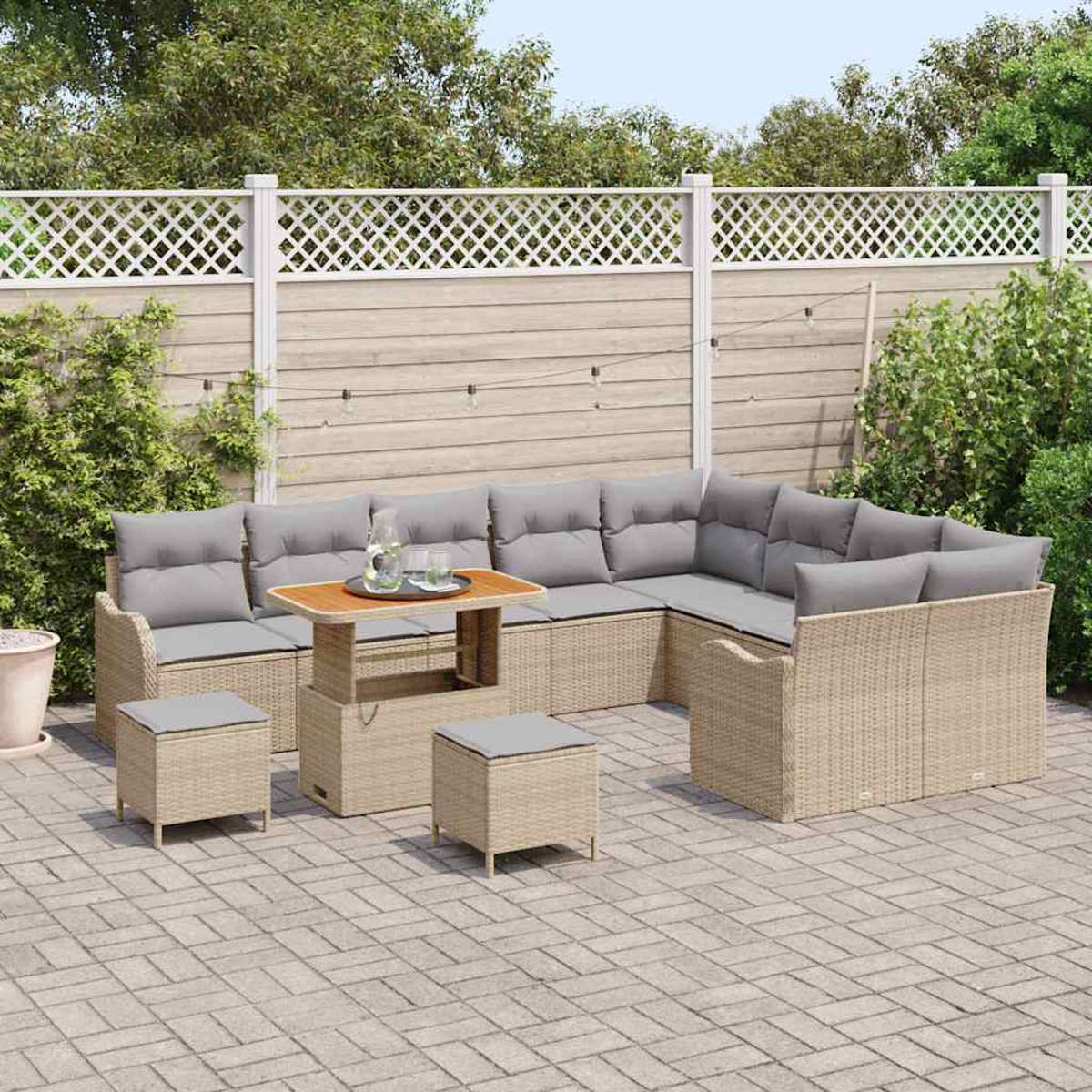 Eine Sitzgruppe im Freien mit grauen Kissen, einem Tisch mit Hubfunktion und zwei Hockern. Auf einer Terrasse mit weißem Zaun und Grün.