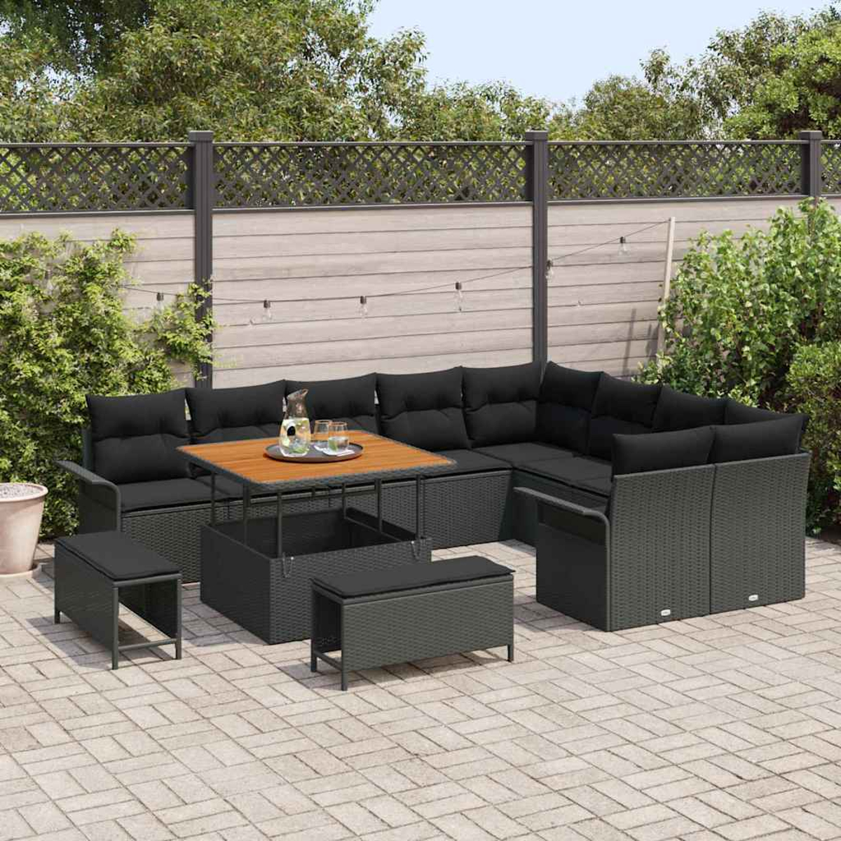 Outdoor-Ecksofa mit schwarzen Kissen, einem Holztisch und zwei Bänken auf einer Ziegelterrasse, mit Zaun und Grün im Hintergrund.