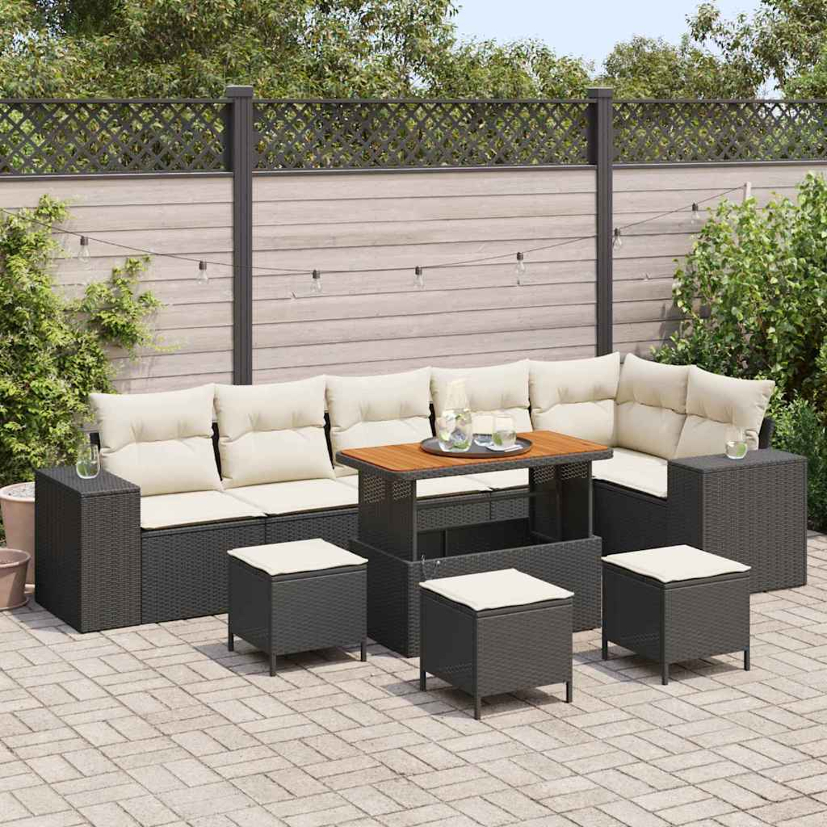 Outdoor-Terrassenset mit dunkelgrauen Korbmöbeln, beigefarbenen Kissen und einem Holztisch. Der Hintergrund zeigt einen Zaun und Grün.