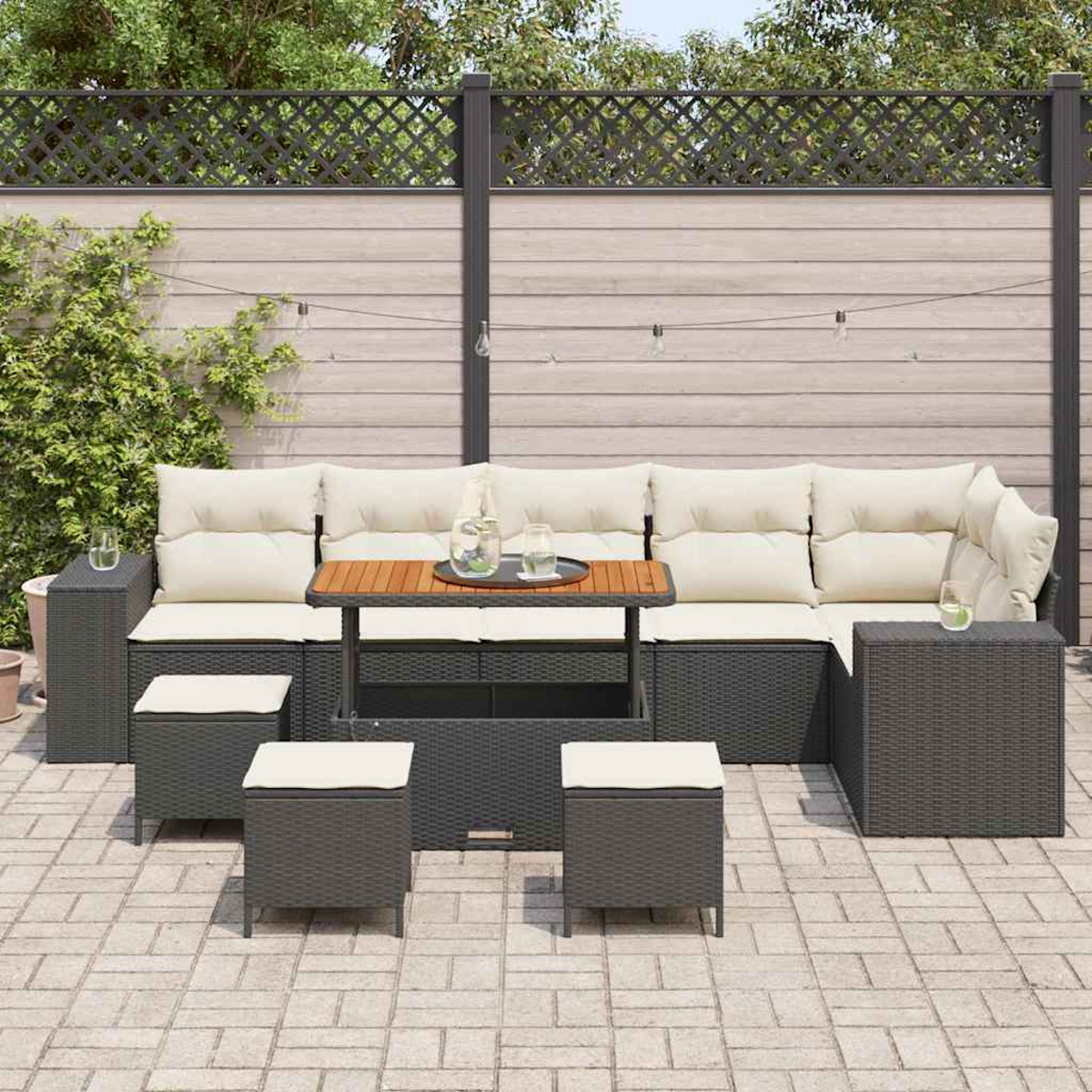 Outdoor-Ecksofa mit Kissen, Tisch mit Getränken und Hockern auf einer Terrasse. Im Hintergrund ein Zaun und Pflanzen.