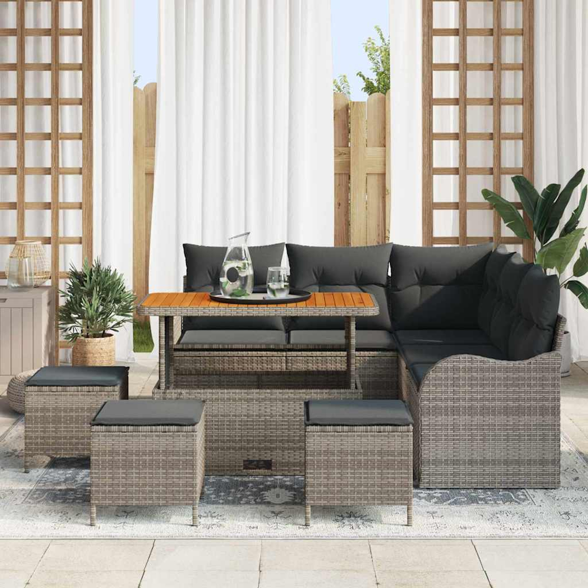 Gartenmöbel-Set aus Korbgeflecht mit Tisch, Ecksofa und Ottomanen. Graue Kissen und eine Tischplatte aus Holz sind sichtbar.