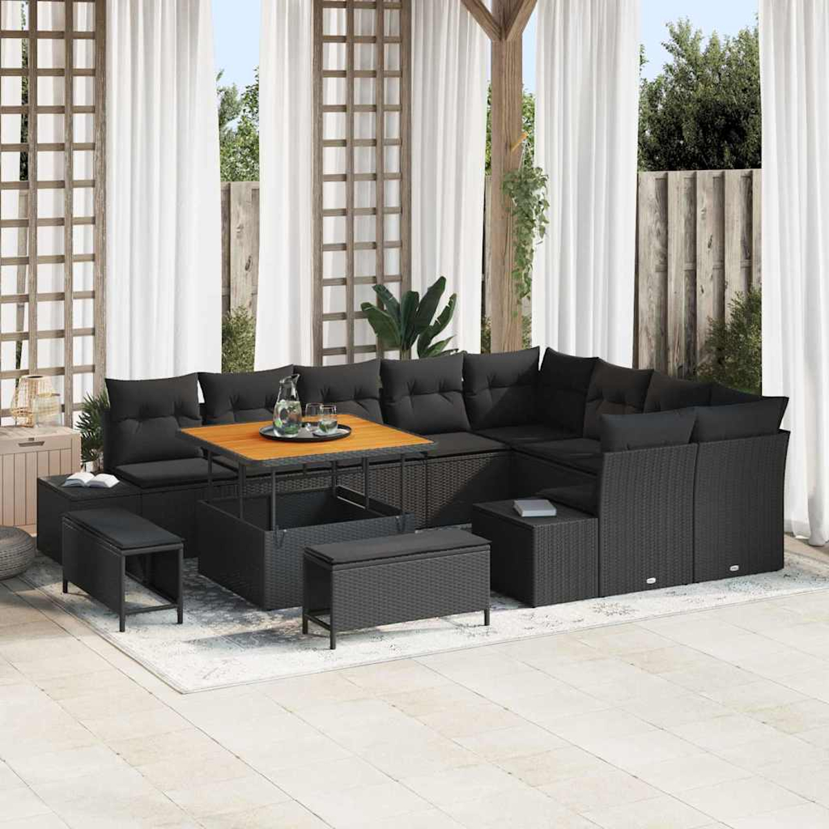 Outdoor-Terrassenset mit schwarzen Korbmöbeln, Kissen und einem Holztisch. Weiße Vorhänge und grüne Pflanzen bilden den Hintergrund.