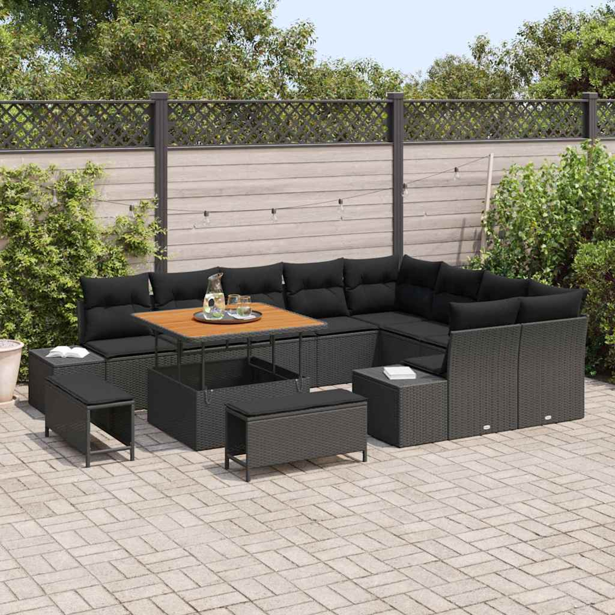 Garten-Lounge-Set mit schwarzen Kissen, Holztisch mit Getränken und Bänken. Hintergrund: Zaun und Grün.