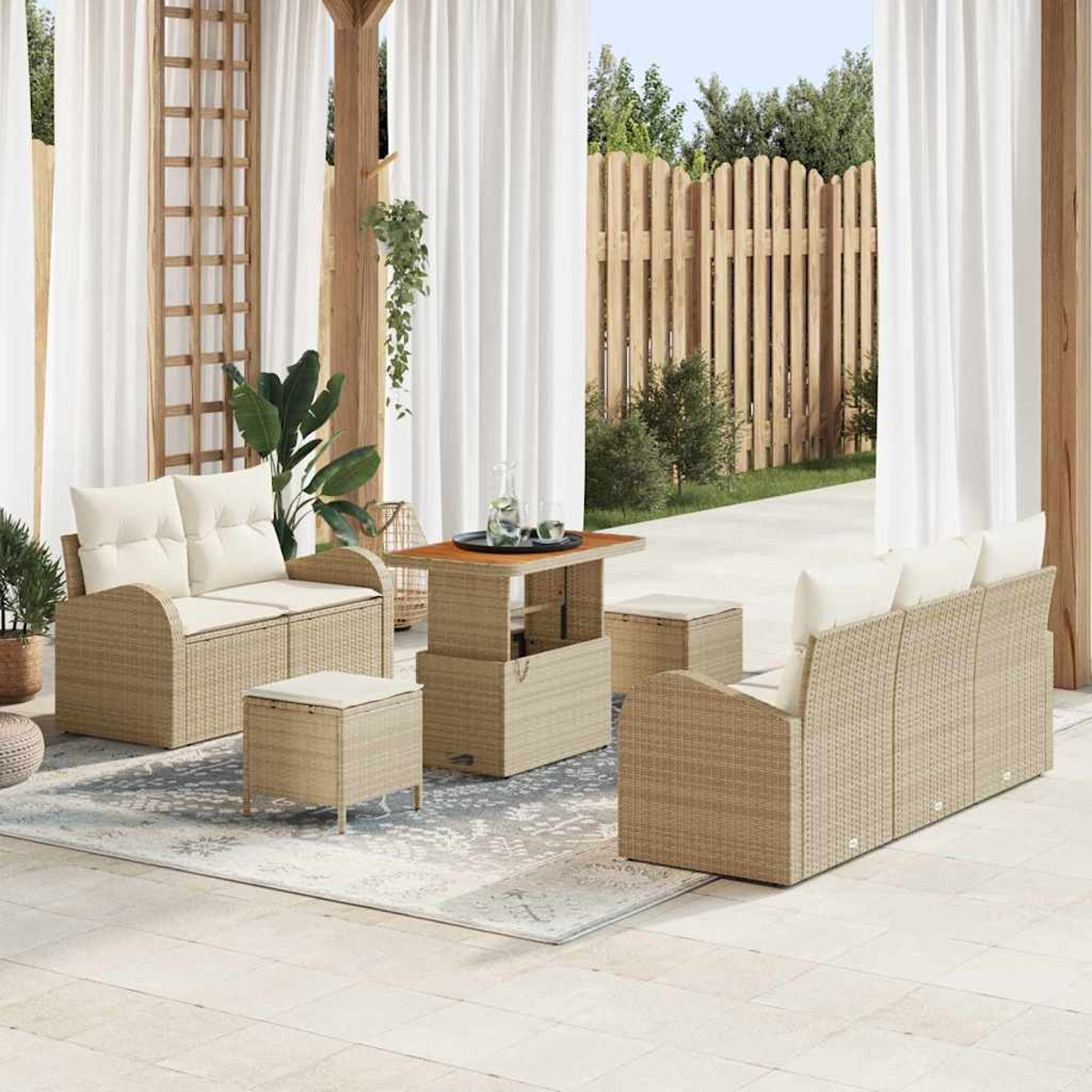 Arredamento da patio esterno con mobili in vimini. Include divani, pouf e un tavolo. Tende bianche, recinzione in legno e piante.