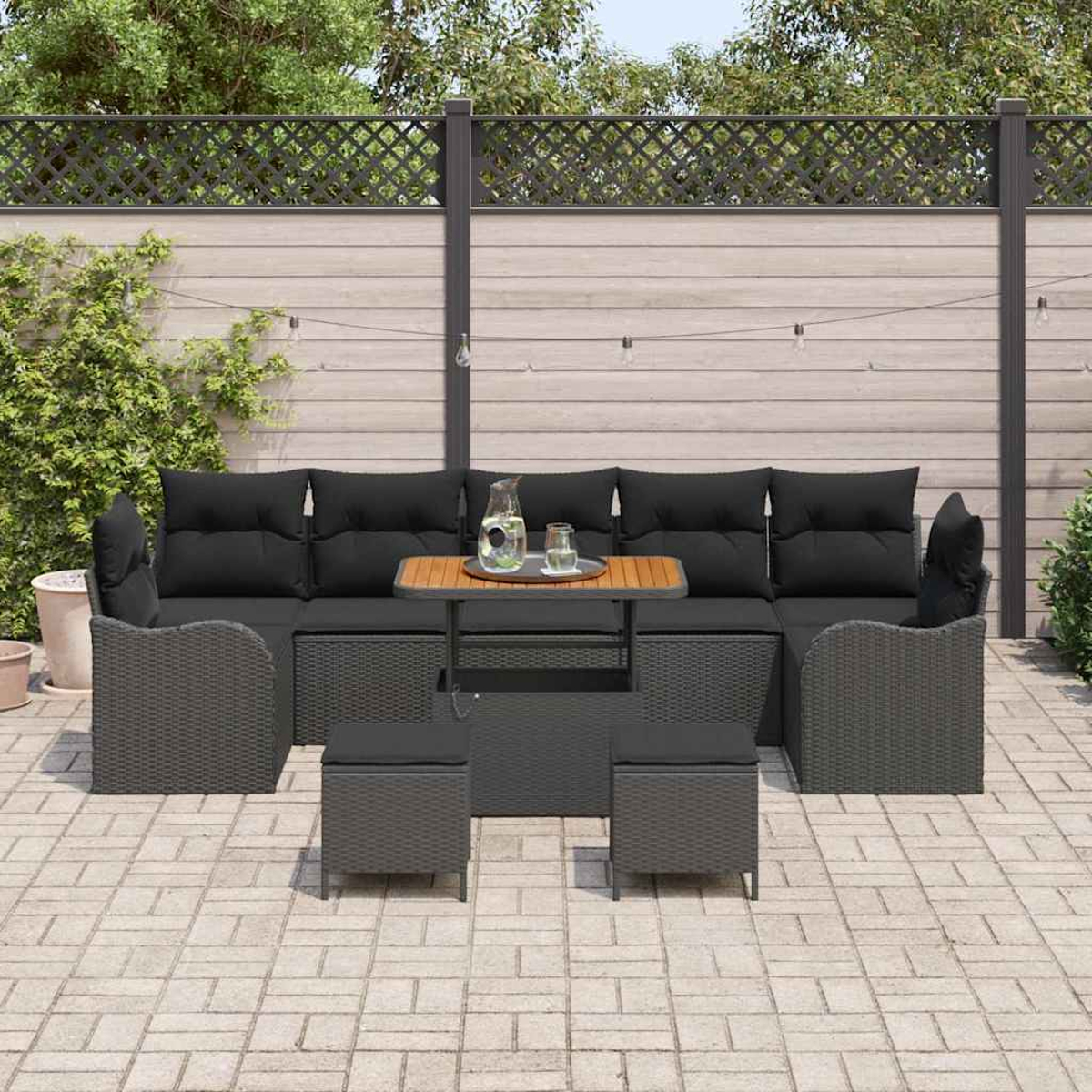 Garten-Sitzgruppe mit schwarzen Kissen und kleinem Tisch auf einer Backstein-Terrasse, mit Holzzaun im Hintergrund.