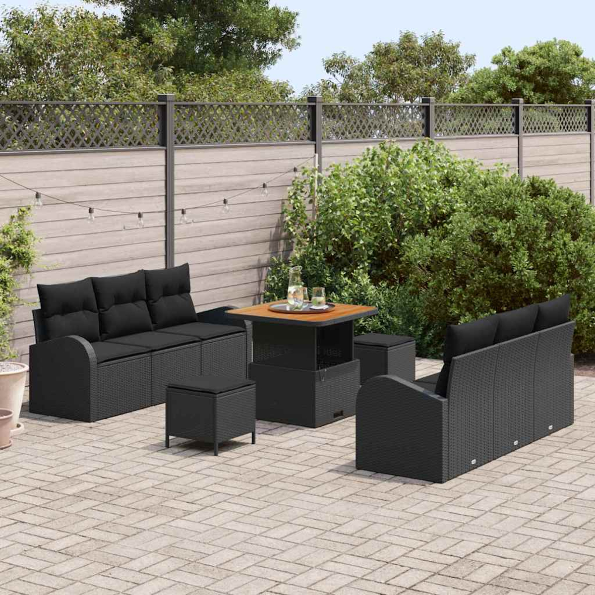Das Terrassenset umfasst ein schwarzes Rattan-Sofa, Stühle, Hocker und einen Tisch mit Getränken auf einer Backsteinterrasse.