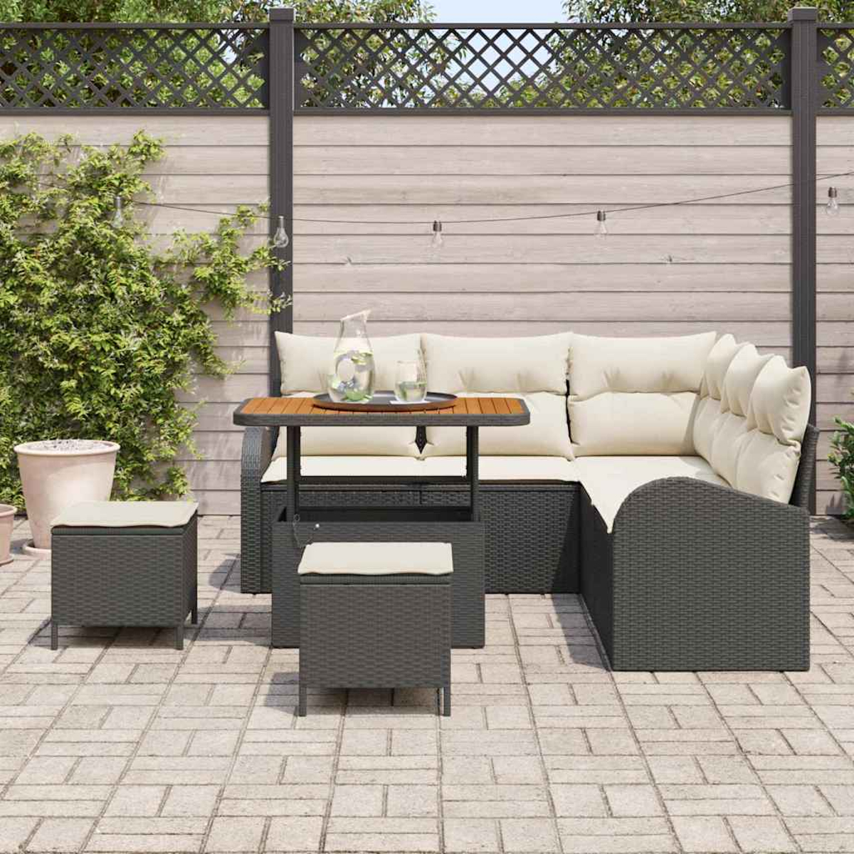 Sitzbereich im Freien mit einem Rattan-Sofa, einem kleinen Tisch und zwei Hockern auf einer Backsteinterrasse.