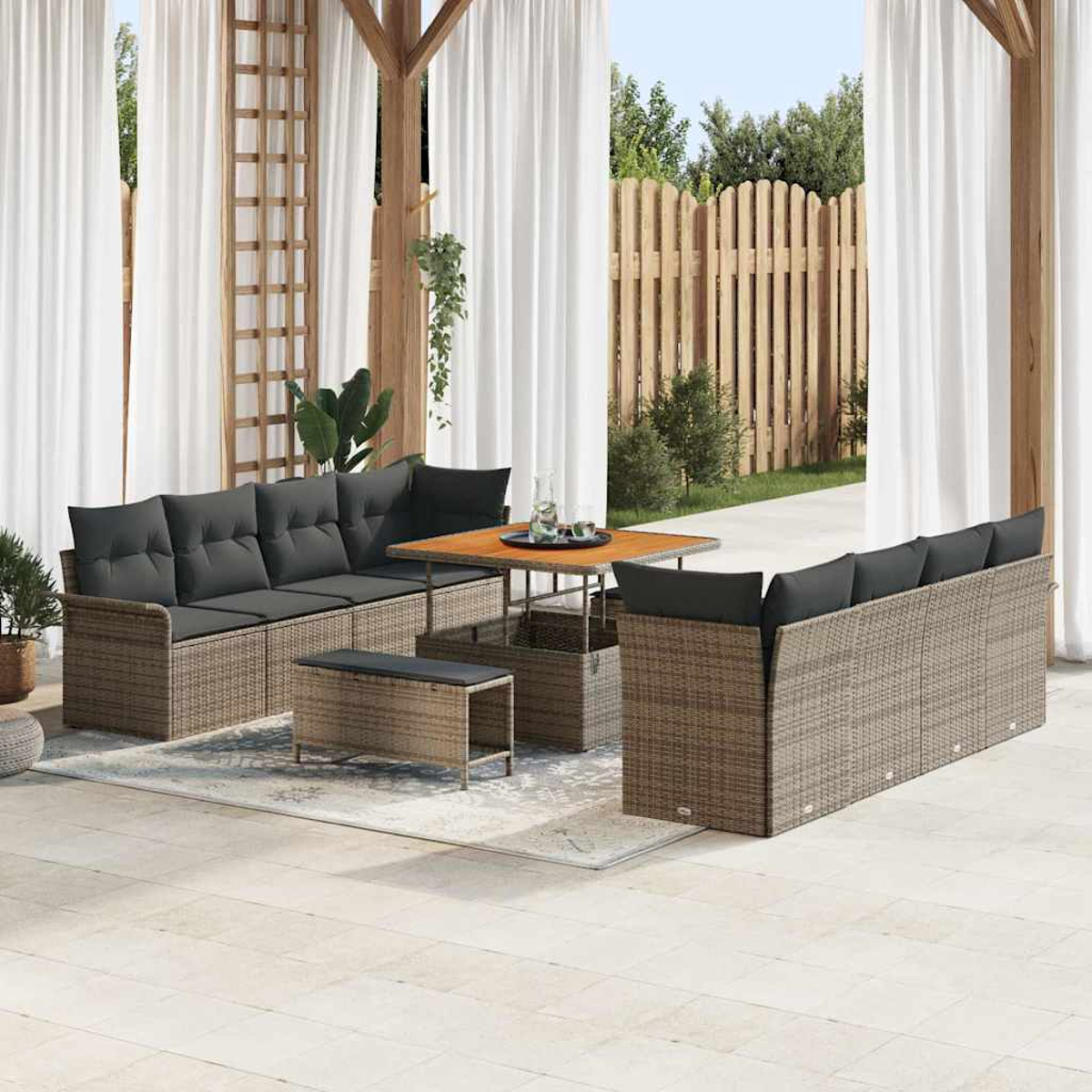 Set da patio esterno con mobili in vimini marrone, cuscini grigi e un tavolo in legno su un tappeto a motivi.