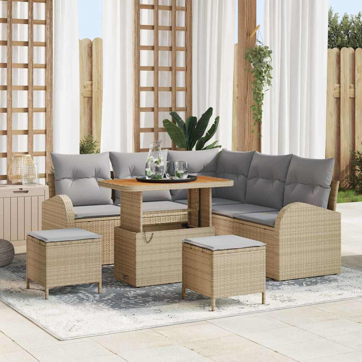 Gartenmöbel-Set aus Korbgeflecht mit grauen Kissen. Enthält einen Tisch, ein Sofa und zwei Hocker auf einem Teppich. Weiße Vorhänge im Hintergrund.