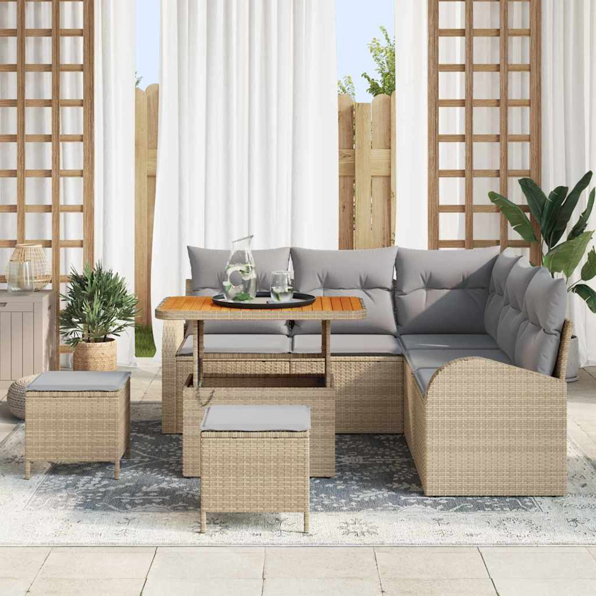 Garten-Sitzgruppe mit Tisch, zwei Hockern und Pflanzen. Graue Kissen auf Korbmöbeln. Weiße Vorhänge und Holzgitter im Hintergrund.