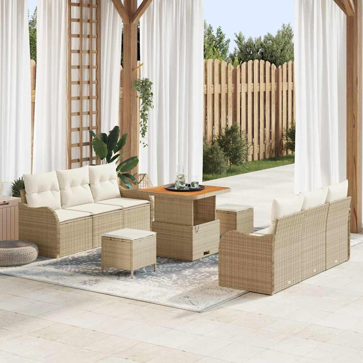 Terrassenset mit beigen Sofas, Ottomanen und Tisch. Weiße Vorhänge und Holzkonstruktion. Im Hintergrund ein Holzzaun und Bäume.