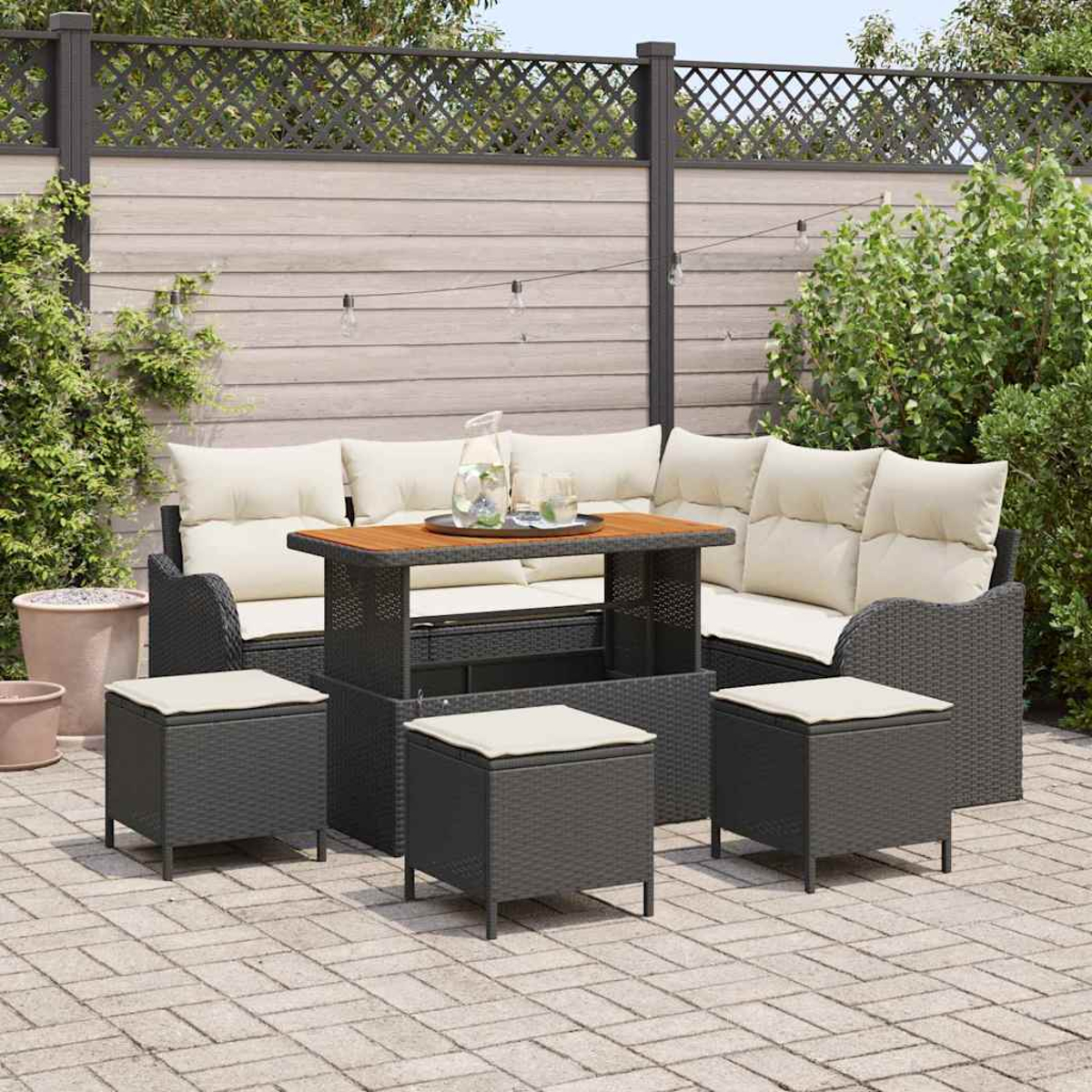 Garten-Terrassenset mit dunkelgrauen Korbmöbeln und cremefarbenen Kissen. Enthält einen Tisch, ein Sofa und Fußhocker auf einer Ziegelterrasse, mit Zaun.