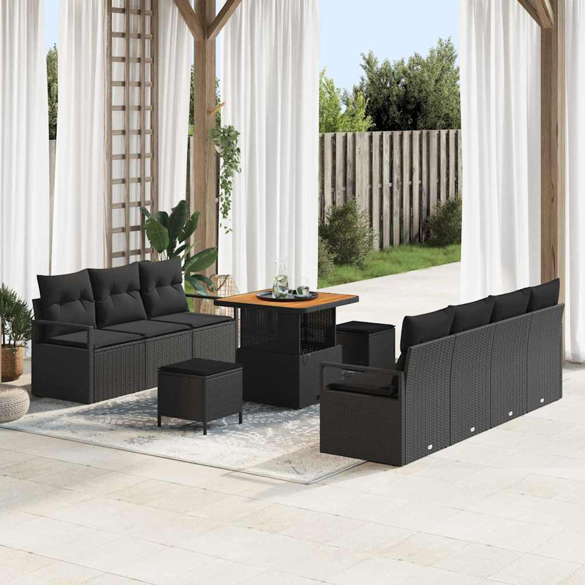 Terrassenmöbel-Set mit schwarzem Korbmöbel, Holztisch und weißen Vorhängen. Hinterhof mit Rasen und Holzzaun sichtbar.