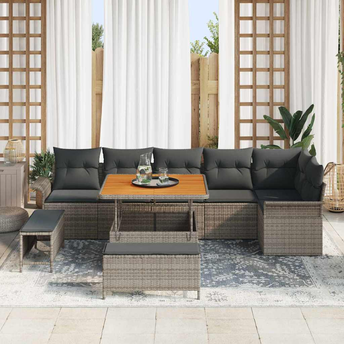 Ein graues Outdoor-Ecksofa mit Holztisch, grauen Kissen und einer Bank. Dahinter ein Fenster mit weißen Vorhängen.