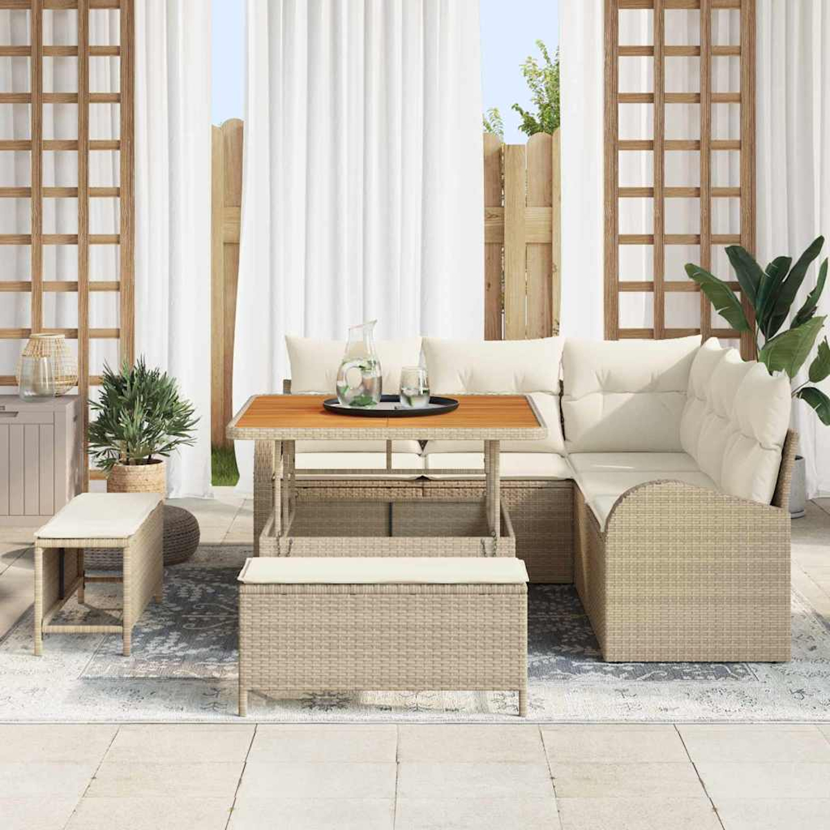 Garten-Sitzgruppe mit Tisch, Bank und Ecksofa. Weiße Vorhänge und Holzgitter im Hintergrund. Pflanzen und Dekoration tragen zum Ambiente bei.