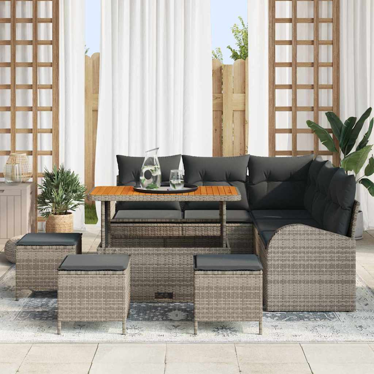 Outdoor-Sofa-Set mit Tisch und Hockern. Graue Kissen, Korbmuster. Pflanzen, Vorhänge, Holzgitter und Zaun im Hintergrund.