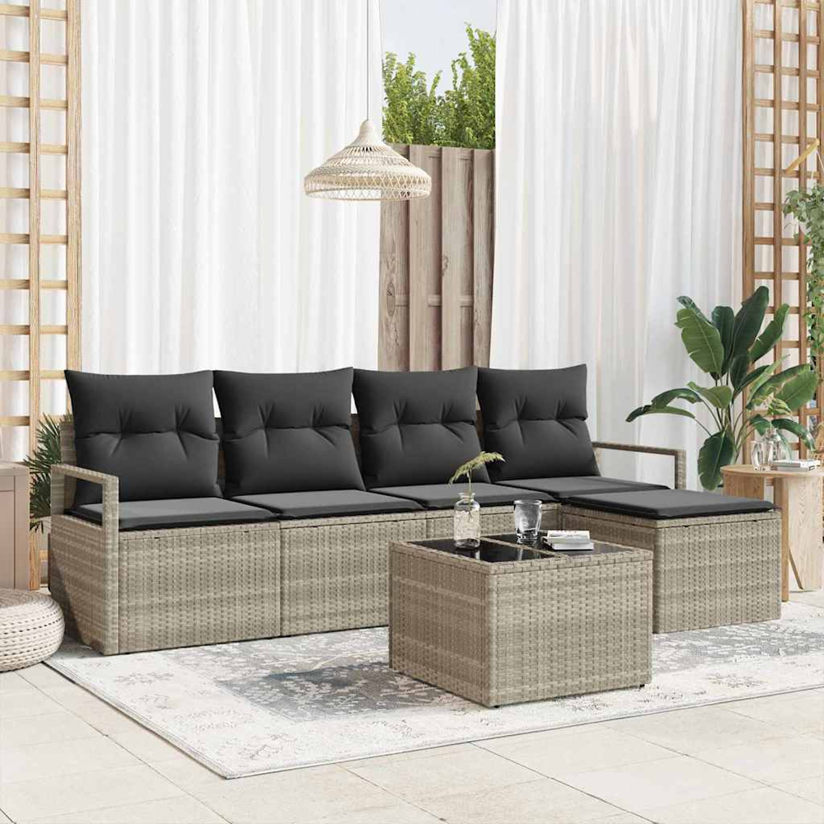Gartenmöbel-Set mit grauen Kissen, quadratischem Couchtisch und Teppich. Weiße Vorhänge und Pflanzen im Hintergrund.