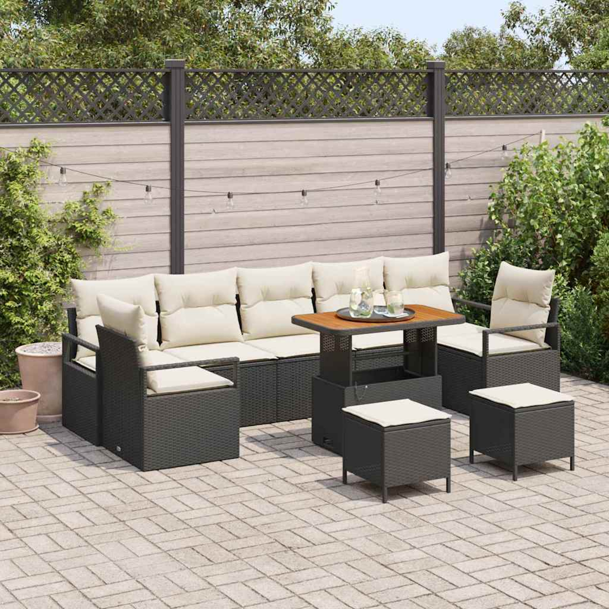 Terrassenset mit Sofa, zwei Stühlen, zwei Hockern und einem Tisch. Beige Kissen auf dunkelgrauen Korbmöbeln. Ziegelterrasse, Holzzaun.