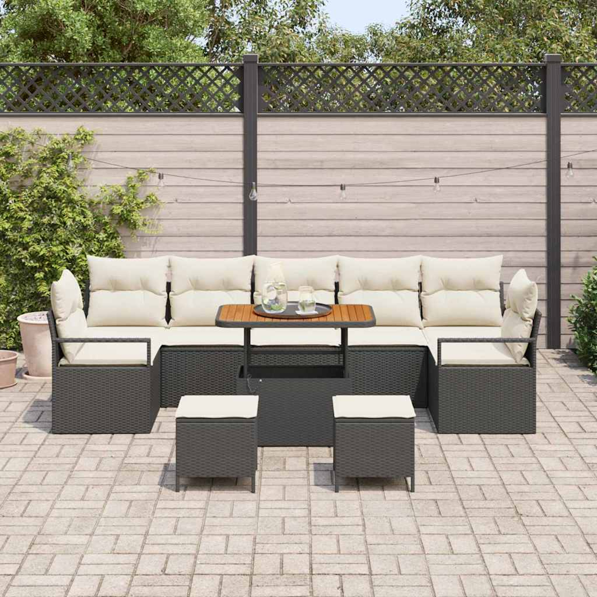Gartenmöbel-Set mit Tisch, Sofa und Hockern auf einer Ziegelterrasse, umgeben von einem Holzzaun und Grün.