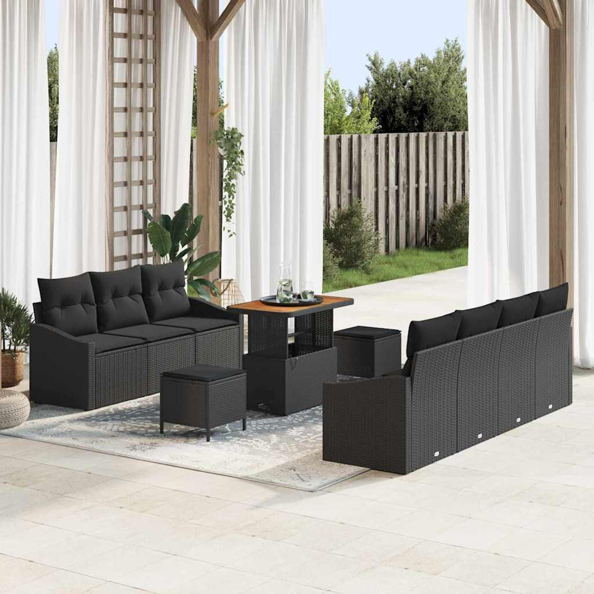 Terrassenset mit schwarzen Korbmöbeln, darunter ein Sofa, Ottomanen und ein Tisch, auf einem hellen Teppich, mit weißen Vorhängen und Gartenblick.