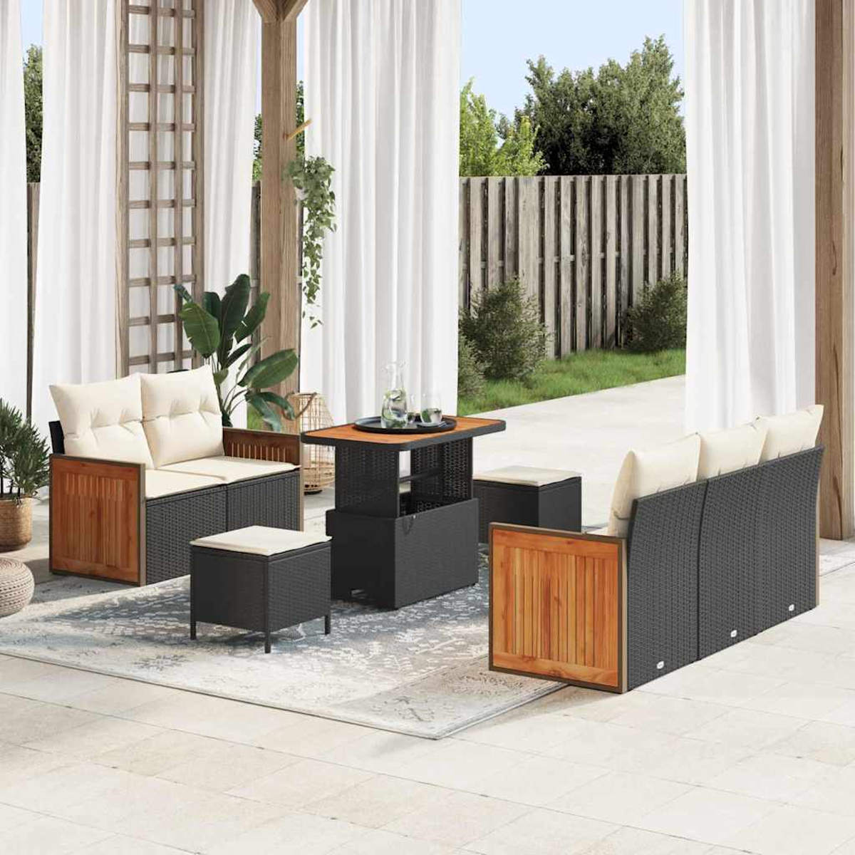 Set da patio esterno. Divano, due sedie, tavolo e due pouf. Cuscini beige e dettagli in legno. Tende bianche sullo sfondo.